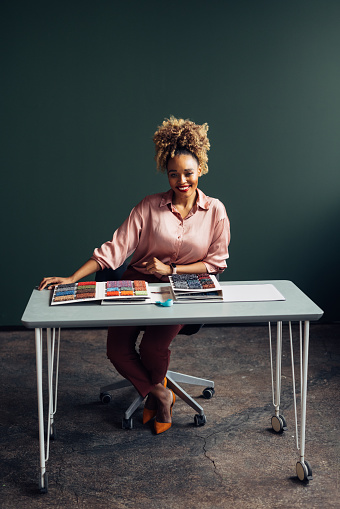A portrait of a smiling African-American interior designer using carpet catalogue while deciding which carpet to use for home decoration. She is sitting at the desk in her office. (copy space)
