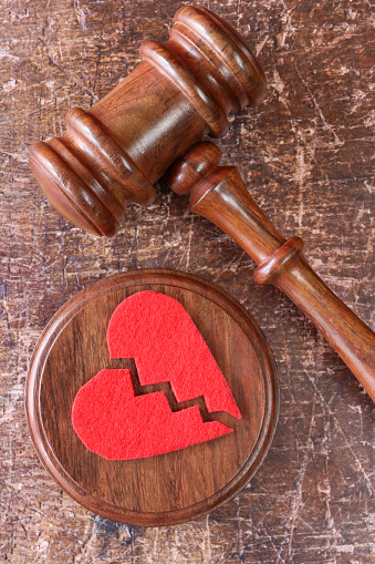 Stock photo showing close-up, elevated view of a hardwood ceremonial mallet and circular sound block with red, broken heart-shape. Divorce and relationship difficulties concept.