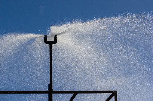 two water sprinklers spraying water with a clear blue sky as a background