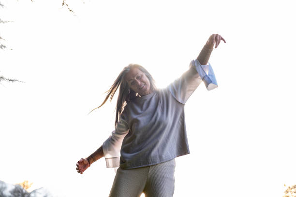 A middle-aged woman practising neurodance on a green lawn in the park at sunset.