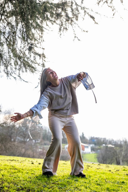 A middle-aged woman practising neurodance on a green lawn in the park at sunset.
