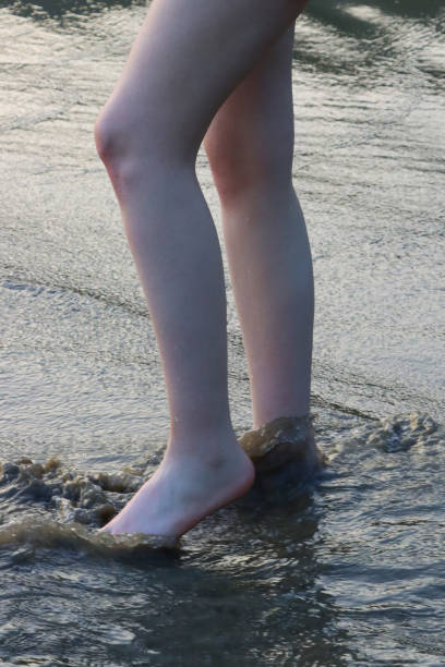 nahaufnahme einer nicht erkennbaren kaukasischen frau, die knöcheltief im meerwasser paddelt, gezeitenwellen, beine und nackte füße, strandsand am meer, fokus auf den vordergrund - human foot wading sea human toe stock-fotos und bilder