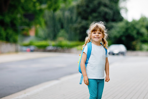 Cute little preschool girl going to playschool. Healthy toddler child walking to nursery and kindergarten. Happy child with backpack on city street, outdoors. City, traffic, safety on school way