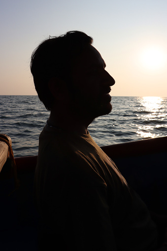 The silhouette of a man in a hat against the background of a bright sunset and the endless sea. A thoughtful adventurer, thoughts about the future and the meaning of life.