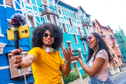 African influencers recording an online video using phone and mic while visiting a colorful street