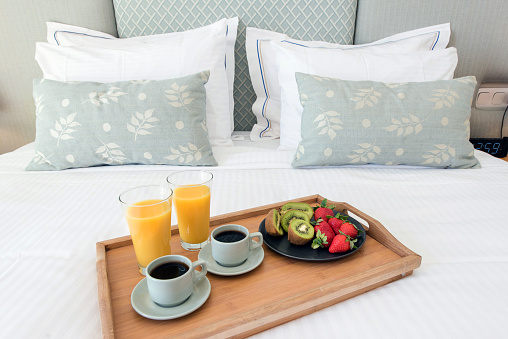 2 cups of coffee, orange juice and fruits served on a tray in a hotel bedroom