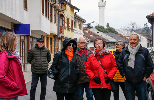 A medium group of people are exploring the Konjic city.  They watch what the tour guide shows them. Group of friends in good spirits are walking on the city street