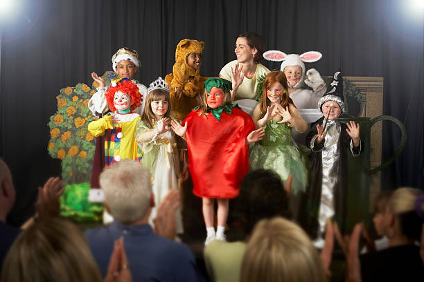 children (4-9) wearing costumes and teacher waving on stage - theater publiek stockfoto's en -beelden