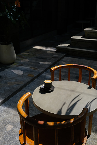 Black cup of coffee with milk foam on top view on cement table with light shading and shadow of leaf. empty cafe