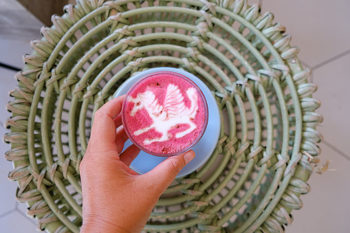 Woman holding healthy trendy beetroot latte with latte art in ceramic cup on wooden table. Top view.
