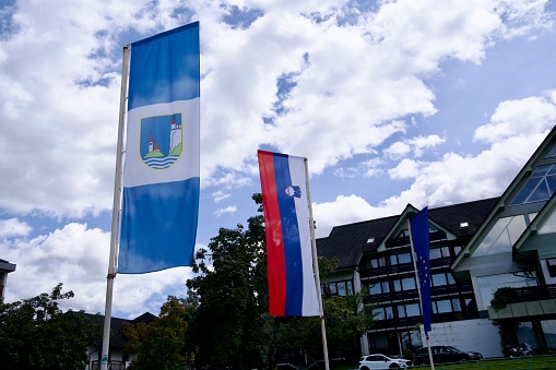 Waving flags at center of Slovenian City of Bled on a blue cloudy summer day. Photo taken August 8th, 2023, Bled, Slovenia.