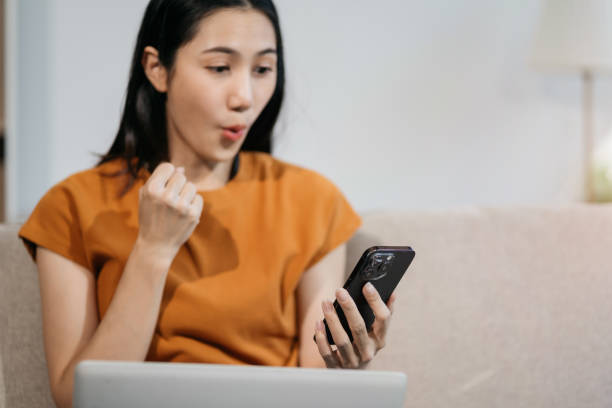 istock Excited woman work distant on computer talk on cellphone celebrate online win. Happy young female use laptop feel euphoric overjoyed triumph with good news over smartphone call. 2002486759