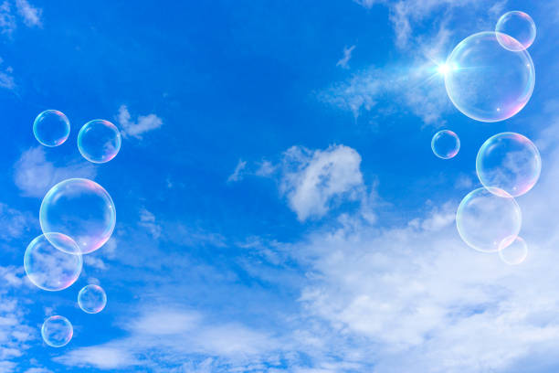 Young girl playing blowing soap bubbles in a park with a blue sky background and white clouds Joke that resubmits childhood.For now it blows and for now the stick is handled with your hands and with a certain speed the bubbles are formed in contact with the air.