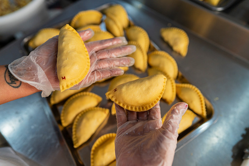 Employees in a small food business specializing in empanadas, dressed in uniform, are in the business kitchen preparing the implements they use for the day's preparation.