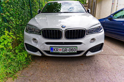 Close-up front view of white BMW luxury car with Slovenian license plate at lakeshore of Lake Bled on a cloudy summer day. Photo taken August 8th, 2023, Bled, Slovenia.