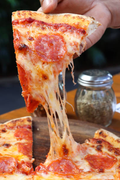 istock Full frame close-up image of pepperoni pizza slice being raised from plate by hand, melted golden buffalo mozzarella cheese and rich tomato marinara sauce stretching and oozing from the hot food, chili and herbs in background 2002509374