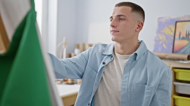 A focused young man in casual clothing attentively working on a creative project indoors.