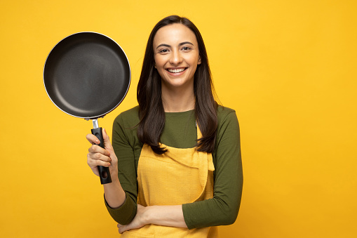 Photo of pretty positive young woman in yellow apron isolated on yellow backgroundPhoto of pretty positive young woman holding frying pan in yellow apron isolated on yellow background