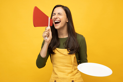 Photo of pretty positive young chef woman announcement message in yellow apron isolated on yellow background