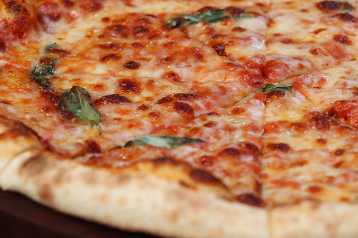 Stock photo showing close-up image of a sliced Margherita pizza, with a tomato marinara base and large stone baked crust, garnished with dried basil leaves, and mozzarella cheese, Italian food