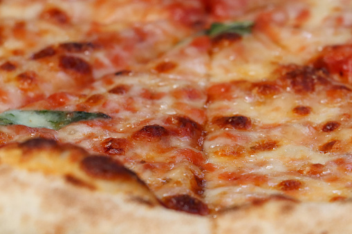 Stock photo showing extreme close-up image of a sliced Margherita pizza, with a stone baked crust, garnished with dried basil leaves, and mozzarella cheese, with a tomato marinara base