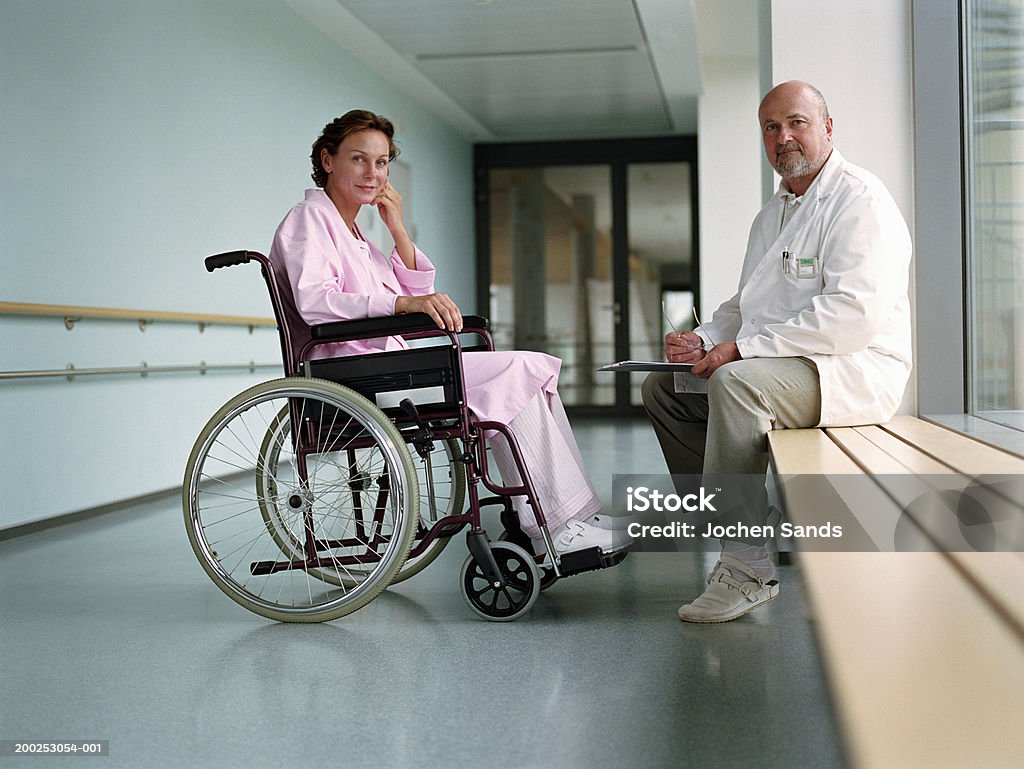 Mature male doctor by female patient in wheelchair, smiling, portrait  Bathrobe Stock Photo