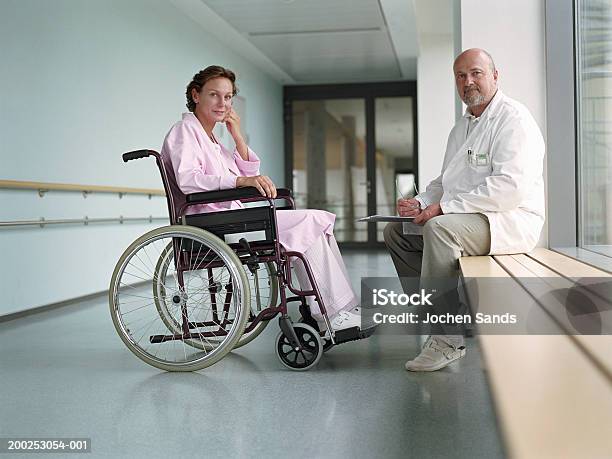 Mature Male Doctor By Female Patient In Wheelchair Smiling Portrait Stock Photo - Download Image Now