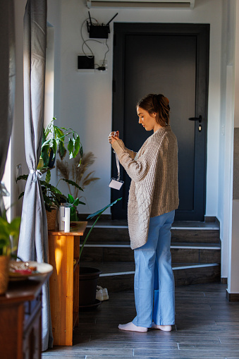 Full length shot of young woman standing in her hallway and putting on her ID card before heading out to work.