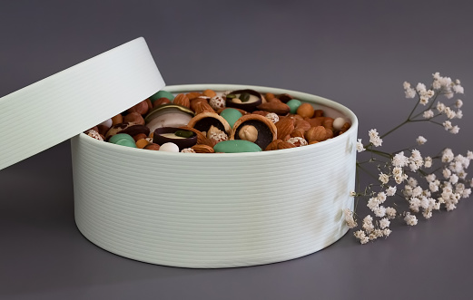 On a light background there is a round box filled with various nuts and dried fruits. Mothers Day. Valentine's Day. International Women's Day.A delightful gift. Low-fat food.