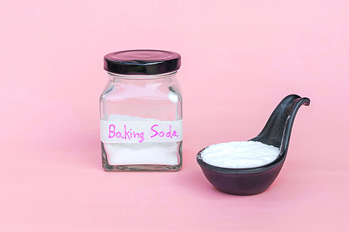 Jar and spoonful of baking soda isolated on pink background