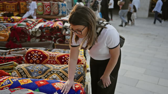 A young woman examines colorful textiles at souq waqif, a traditional market in doha, qatar, showcasing vibrant local craftsmanship.