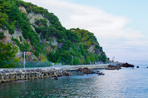 Gangneung City, South Korea - July 29th, 2019: Heonhwa Road winds along rocky hillsides with calm East Sea waters below, showcasing the serene beauty of South Korea's closest road to the sea.