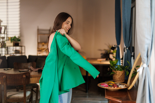 Young woman looking in the mirror and putting on a green blazer