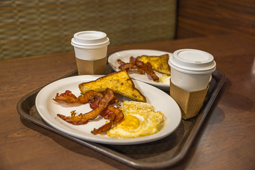 Close-up view of breakfast tray at Miami Airport, showcasing baked bacon, eggs, and coffee in a disposable cup.