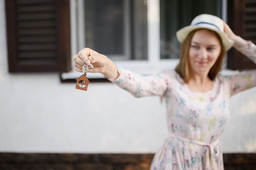 Happy young woman in front of a new house with the keys to a new house, focus on the keys. The concept of real estate, ownership, rental housing.