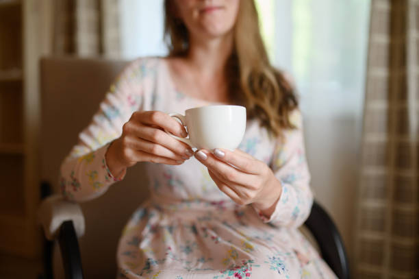 Happy woman sitting down indoors with a coffee. Focus in on the cup and hands.