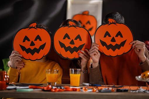 Portrait of mother and her two teenage boys holding Jack o' Lantern masks over their faces and smiling at camera while doing crafts for Halloween.