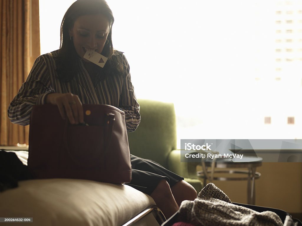 Mature woman looking in purse in hotel room, card key in mouth  40-44 Years Stock Photo