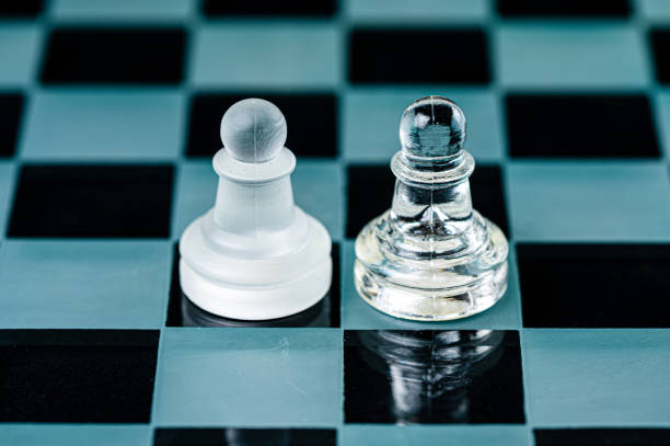 two opponent glass chess pawns on a glass chess board, black background, copy space