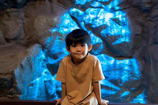 Little Asian boy sits against a rock background, blue lights splashing the background.