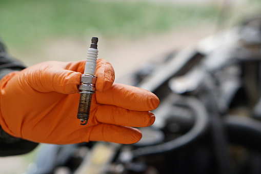 Close up mechanic hands hold old spark plug, spare part of car engine. Concept, machine maintenance, fix, repair, check or diagnose automobile problems by engine specialist.