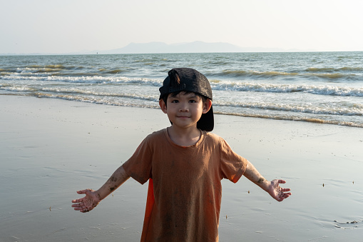 Little Asian boy playing in the sand at the sea beach