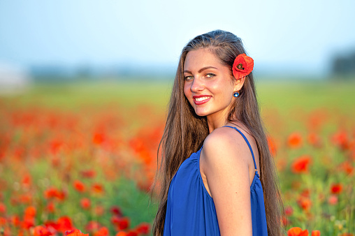 portrait of elegant young woman with long hair in poppy field in evening sunlight