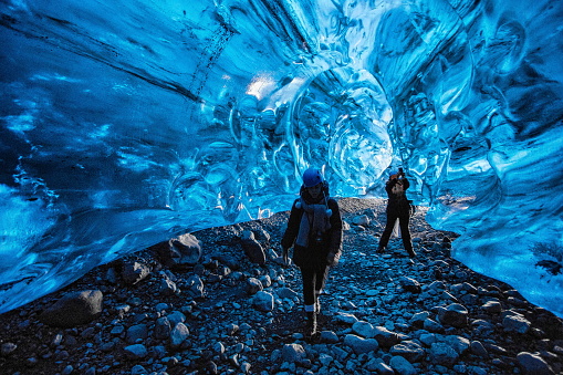 Vatnajokull Glacier, Iceland - March 5, 2020: Two young ladies are walking inside the bluish ice tunnels of Vatnajokull Glacier. Vatnajökull is the largest and most voluminous ice cap in Iceland. Due to rising global temperatures and could be completely gone in 200 years, scientists say.