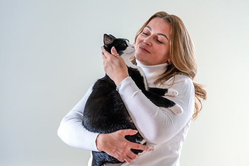 A woman gently hugs her cat, holding him in her arms on a white background