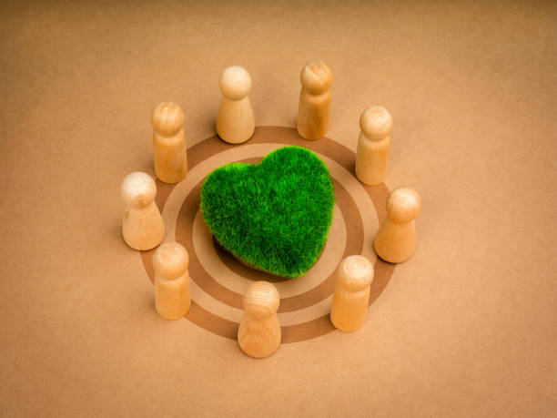 istock Teamwork, revitalizing volunteer group, collaboration community sustainability, environment responsibility concepts. Green heart with wooden people figures on target icon, recycle paper background. 2002776588
