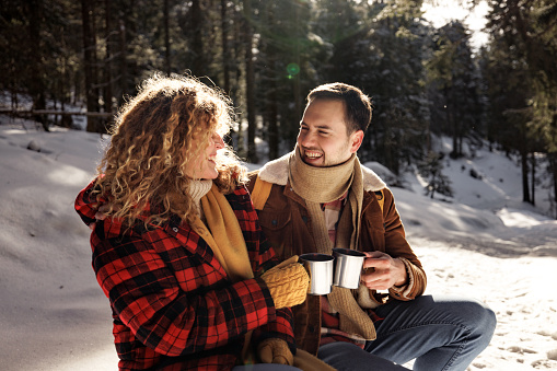 Young cheerful couple enjoying coffee on sunny winter day in the mountain