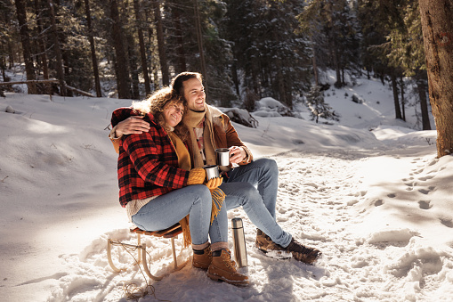 Young cheerful couple enjoying coffee on sunny winter day in the mountain
