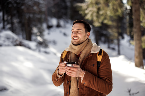 Young handsome man enjoying hot drink on sunny winter day in nature