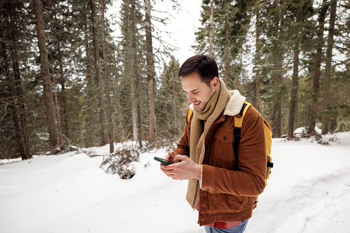 Young handsome man using smart phone in nature during winter day